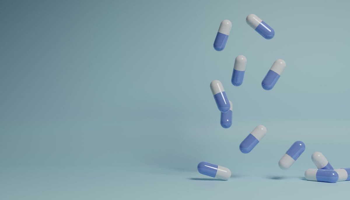 Pale blue and white capsules tumbling through the air against a soft blue background