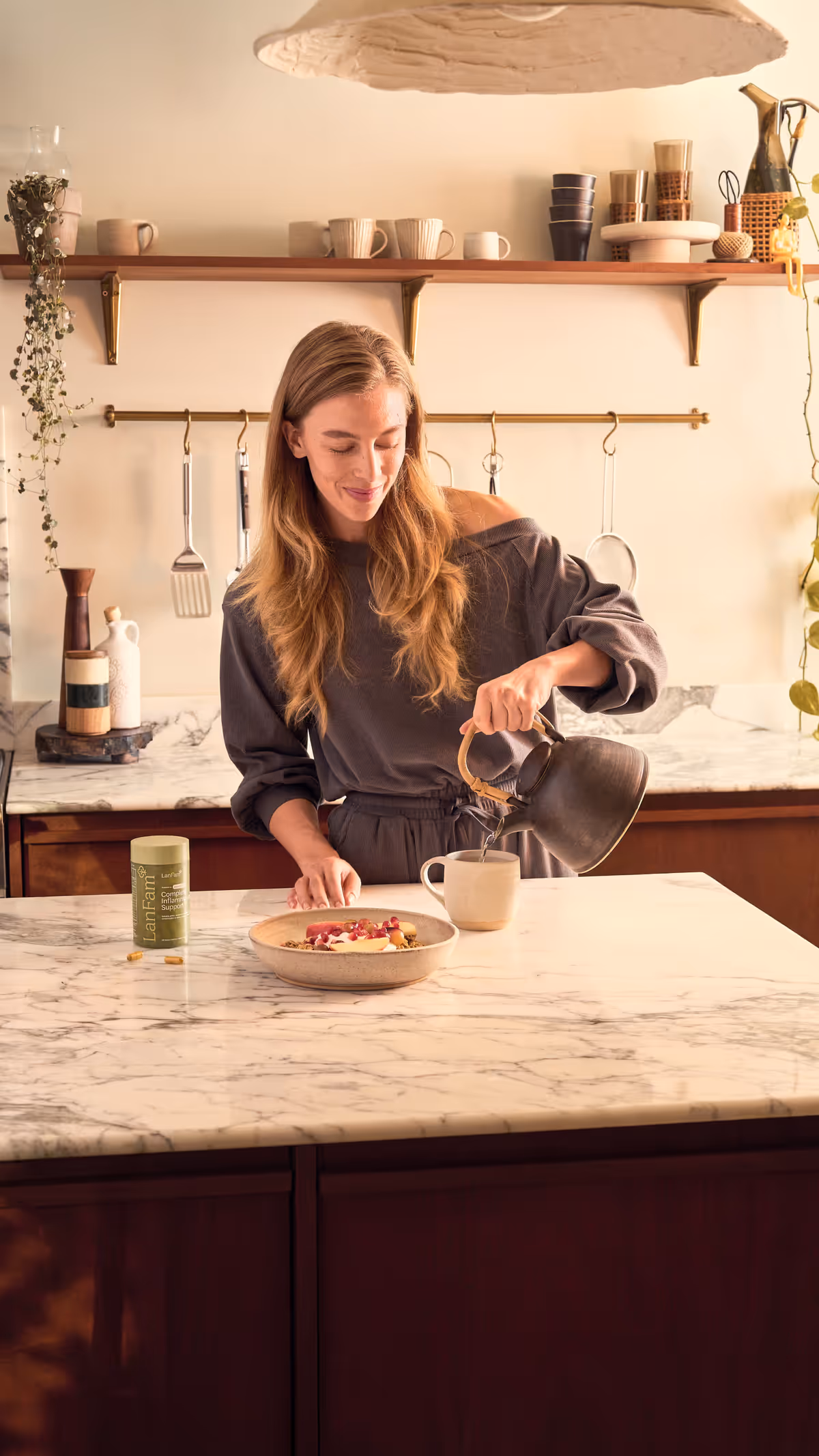 A woman pouring from a kettle at a marble kitchen island, a ProleevaMax jar beside the bowl