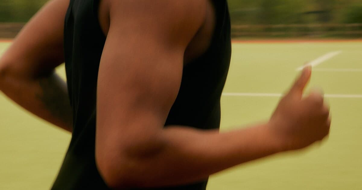 Runner mid-stride on an olive-green court, arm swinging in motion